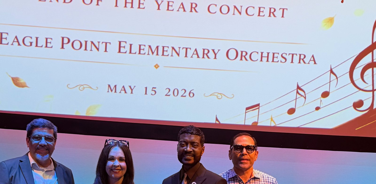 Ricardo with concert organizers in front of the Eagle Point Elementary Orchestra program screen
