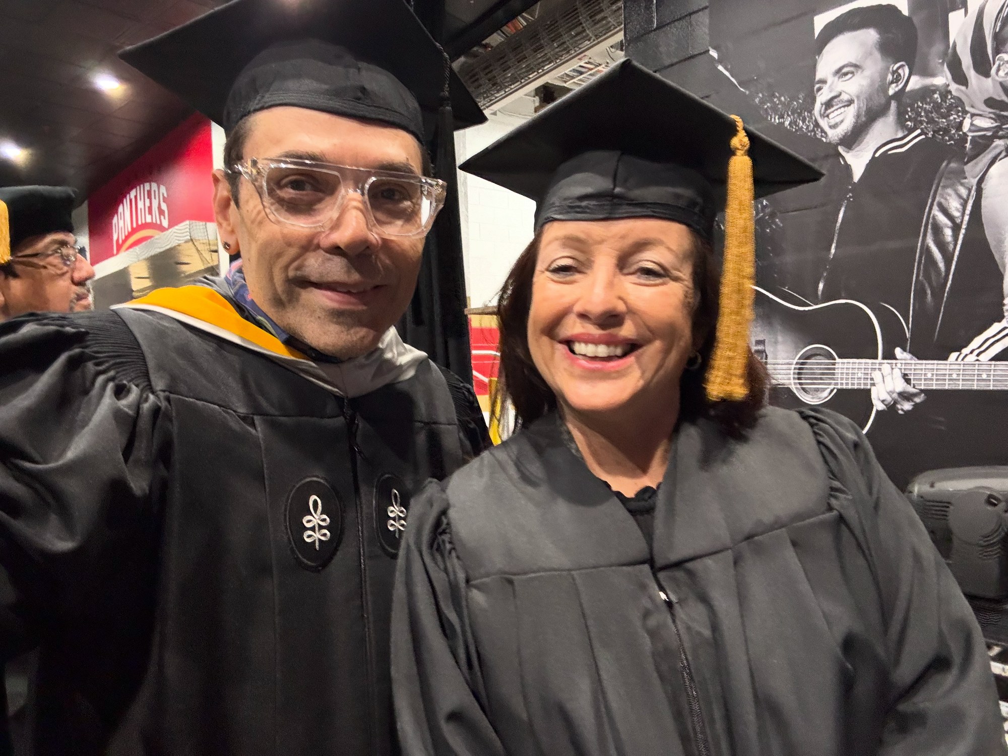 Two faculty members in academic regalia smiling at a graduation ceremony