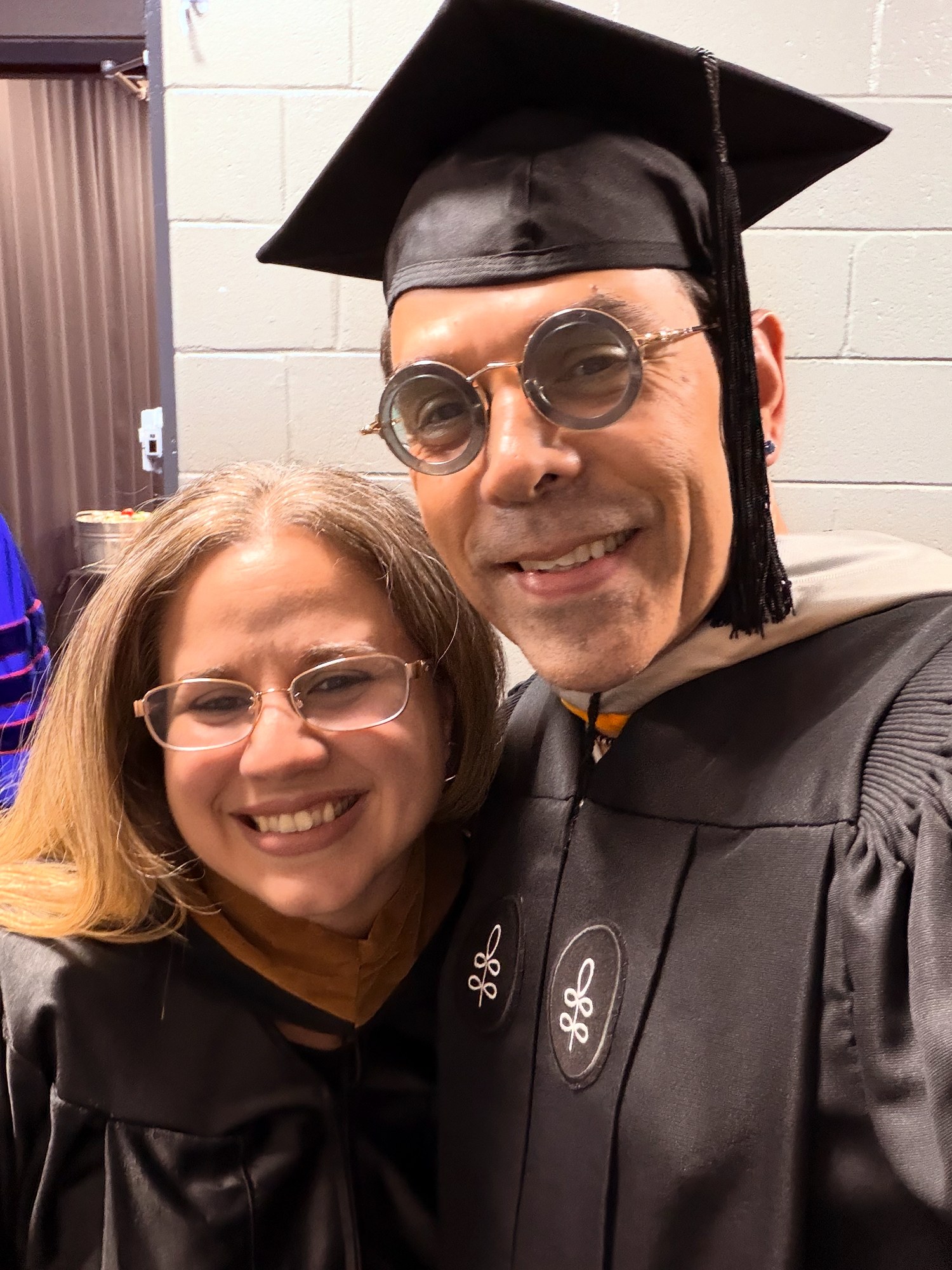 Faculty member in academic regalia posing with a colleague at graduation