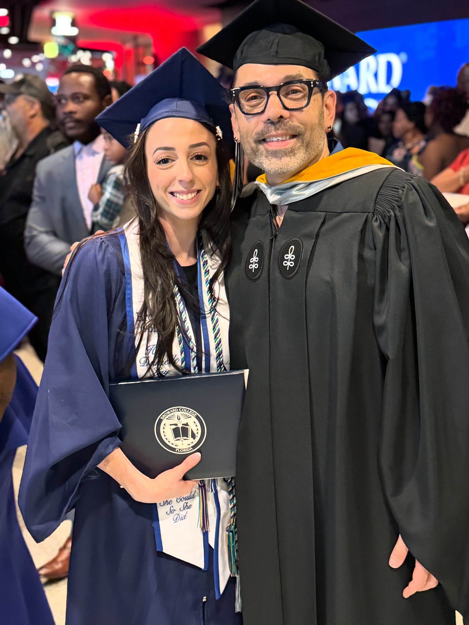 Broward College graduate holding diploma cover with faculty member at commencement